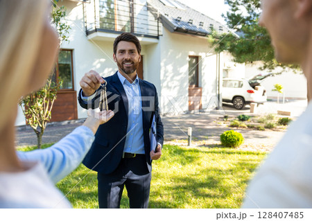 A cute young couple getting keys from the real estate agent and looking excited A cute young couple getting keys from the real estate agent and looking excited 128407485