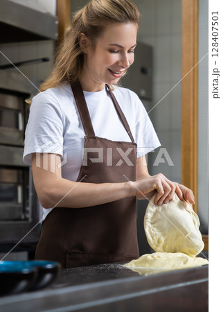 Smiling female baker holding a bowl of dough in a cheerful bakery environment 128407501
