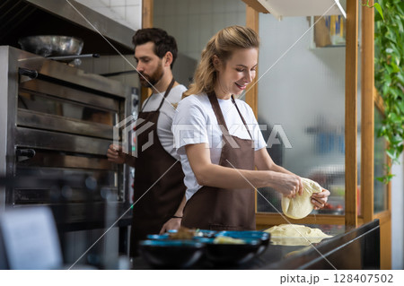 A man and woman prepare dough together in a modern bakery 128407502