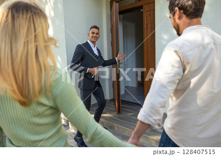 Realtor guiding couple inside modern residence with open door 128407515