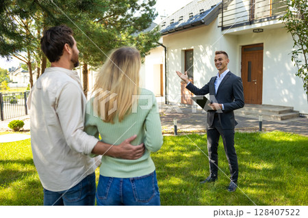 Real estate agent presenting modern house to couple in sunny yard 128407522