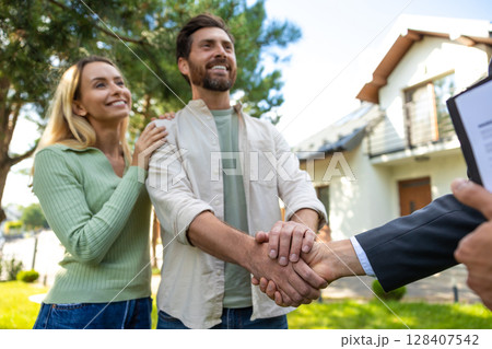 Couple shaking hands with real estate agent outside modern home Couple shaking hands with real estate agent outside modern home 128407542