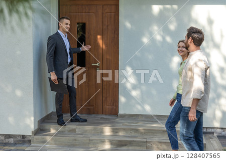 Agent showing house entrance to clients in suburban setting 128407565