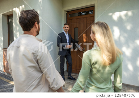 Real estate agent opening door for couple at modern house tour 128407576