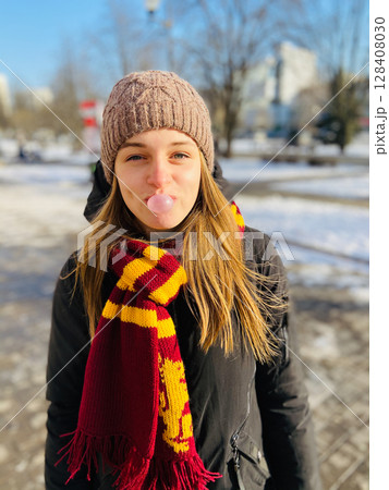 In a Winter Wonderland, a cheerful woman is happily chewing gum in a cozy knit hat In a Winter Wonderland, a cheerful woman is happily chewing gum in a cozy knit hat 128408030