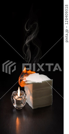 A burning candle lit the napkins on the table 128409318