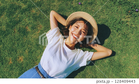 俯瞰で見る芝生に寝転ぶ笑顔の女性と夏の帽子｜笑顔, 夏, 自然	 128409443