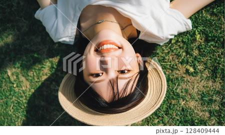 俯瞰で見る芝生に寝転ぶ笑顔の女性と夏の帽子｜笑顔, 夏, 自然	 128409444