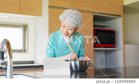 タブレットを見ながら料理するシニア女性 128409869