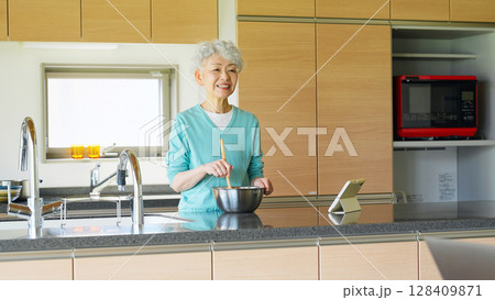 タブレットを見ながら料理するシニア女性 128409871