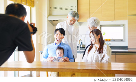 赤ちゃんを囲む三世代家族を撮影するカメラマン 128409896