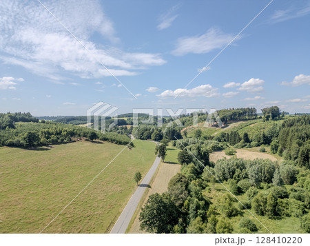 Thommen, Liege, Belgium, A scenic landscape with a winding road and lush green fields under bright 128410220