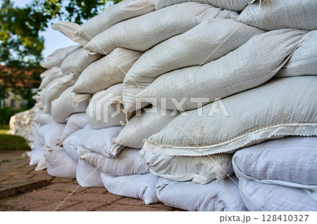 Rows of sandbags stacked as flood barrier on city street. Emergency protection measure to prevent water damage during storms, heavy rain or floods 128410327