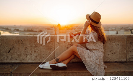 Portrait of happy woman tourist in hat at dawn enjoys cityscape. concept of an active lifestyle. 128411103