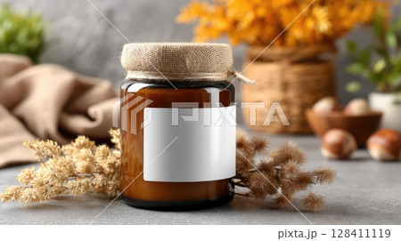 An amber glass jar with a blank label sits on a table, surrounded by autumn decor, creating a cozy, welcoming vibe 128411119