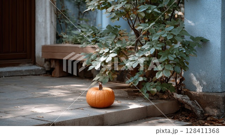 A carved pumpkin grins with its jack-o-lantern face, casting a warm glow in front of an old house on a dark Halloween night 128411368