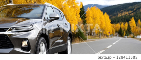 Black SUV navigates a scenic road surrounded by bright yellow trees during autumn, showcasing the beauty of fall foliage 128411385