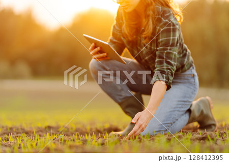 Farmer woman in boots checks the quality of the soil before sowing in her hands with digital tablet. 128412395
