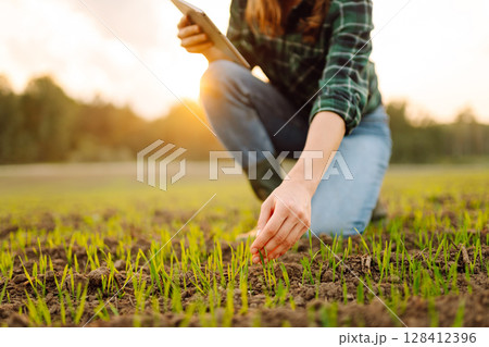 Farmer woman in boots checks the quality of the soil before sowing in her hands with digital tablet. 128412396