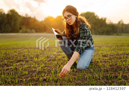 Farmer woman in boots checks the quality of the soil before sowing in her hands with digital tablet. 128412397