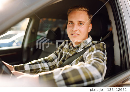 Portrait of handsome young man sitting in the driving seat of his car. Car travel, lifestyle concept Portrait of handsome young man sitting in the driving seat of his car. Car travel, lifestyle concept 128412682