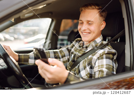 Man using smartphone while sitting in car parked in urban area during daytime. Lifestyle concept. 128412687
