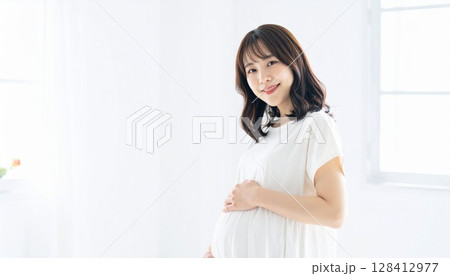 白い部屋で白い服を着たロングヘアーの妊婦のポートレート 白い部屋で白い服を着たロングヘアーの妊婦のポートレート 128412977