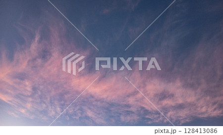 Soft clouds floating across a clear blue sky at sunset 128413086