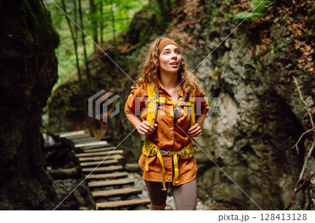 Happy woman in hiking clothes walks along wooden hiking path in mountains. Outdoor adventure concept Happy woman in hiking clothes walks along wooden hiking path in mountains. Outdoor adventure concept 128413128