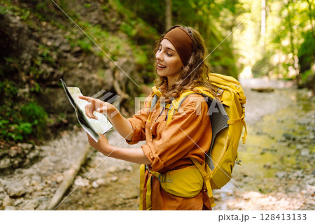 Young woman on a mountain path with a map in her hands, exploring hiking trails. Adventure concept. 128413133
