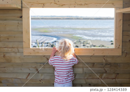 Blonde girl watching birds through a window in a birdwatching hut Blonde girl watching birds through a window in a birdwatching hut 128414389