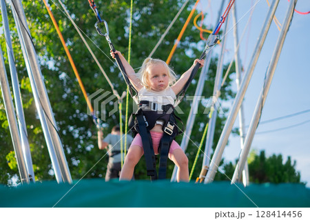 Little European Girl Learning to Jump on a Trampoline with Safety Harness. Summer Fun 128414456