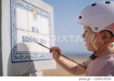 Little Girl in a Bike Helmet Learning to Read a Street Sign 128414504