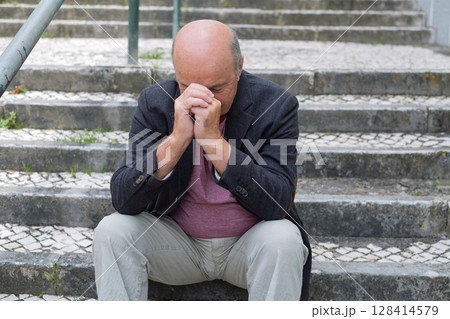 Elderly Spanish Man Sitting on Outdoor Stairs, Lost in Thought, Feeling Tired and Hot 128414579