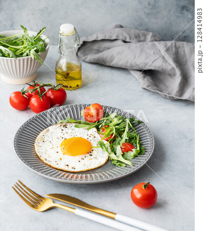 Fried eggs with arugula and cherry tomatoes on a dark plate on a blue txtured background Fried eggs with arugula and cherry tomatoes on a dark plate on a blue txtured background 128414983