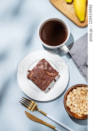 Chocolate banana brownie on a plate on a blue background with a cup of coffee, nuts 128414992