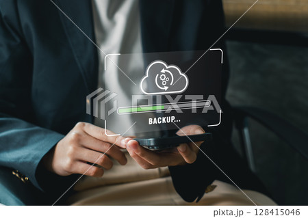 A business professional holds a smartphone displaying a digital backup cloud icon, symbolizing data security and technology. 128415046