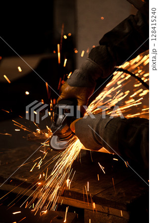 Worker working in industry or factory is holding a cutting stone or grinding stone and sparks are coming out of the metal Worker working in industry or factory is holding a cutting stone or grinding stone and sparks are coming out of the metal 128415240