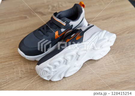 Stylish comfortable and useful grey or blue orange sneakers, on oak wooden floor 128415254