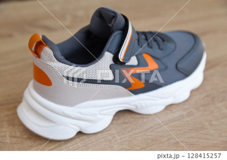 Stylish comfortable and useful grey or blue orange sneakers, on oak wooden floor Stylish comfortable and useful grey or blue orange sneakers, on oak wooden floor 128415257