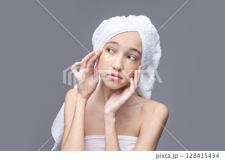 Young asian female applying under eye patches for skincare routine with towel Young asian female applying under eye patches for skincare routine with towel 128415434
