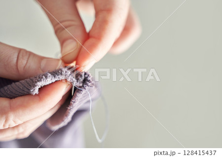 Close-up of adult hands sewing fabric with needle and thread for handcrafted 128415437