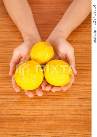 Young Caucasian male holding yellow lemon in hand over brown wooden table 128415514