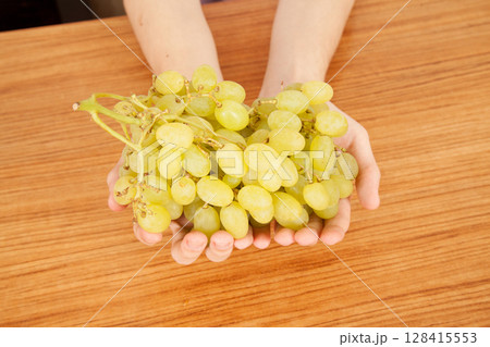 Caucasian man holding bunch of yellow ripe grapes on a wooden table Caucasian man holding bunch of yellow ripe grapes on a wooden table 128415553