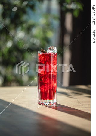 Bright red cocktail with ice cubes in tall glass 128415998