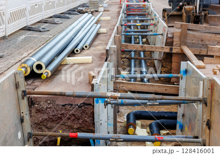 New modern insulated urban pipeline installation construction site exposed underground pipes in shored trenches. Insulated steel pipes lie connection engineering infrastructure upgrade work New modern insulated urban pipeline installation construction site exposed underground pipes in shored trenches. Insulated steel pipes lie connection engineering infrastructure upgrade work 128416001