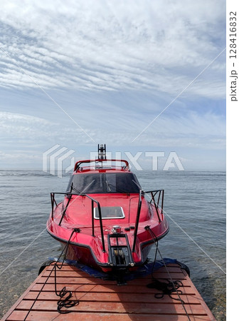 bright red boat docked at serene waterfront with calm waters and clear skies in background. closeup. bright red boat docked at serene waterfront with calm waters and clear skies in background. closeup. 128416832