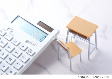 学校の机と椅子、電卓がイメージする、高騰を続けて家計を圧迫する教育費のイメージ 128417220