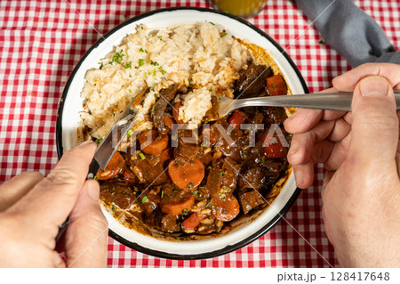 Person eating beef stew with rice using fork and knife Person eating beef stew with rice using fork and knife 128417648