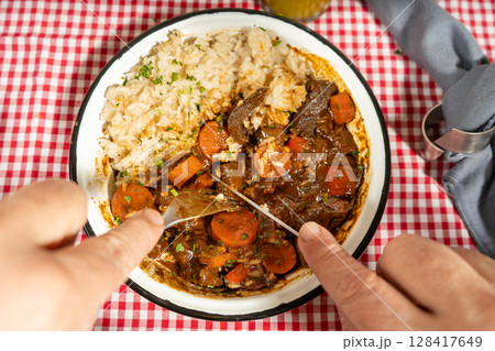 Hands cutting into hearty beef stew with rice 128417649